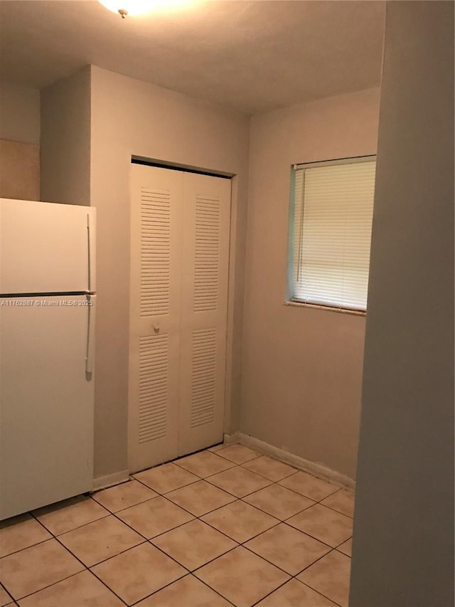 interior space featuring light tile patterned floors, baseboards, a closet, and freestanding refrigerator