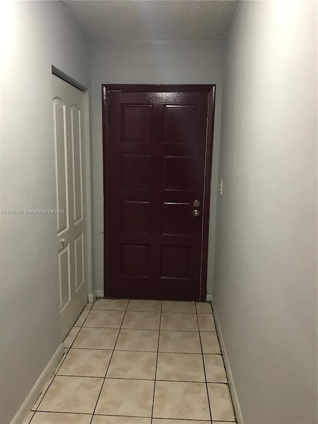 corridor with light tile patterned floors, baseboards, and a textured ceiling