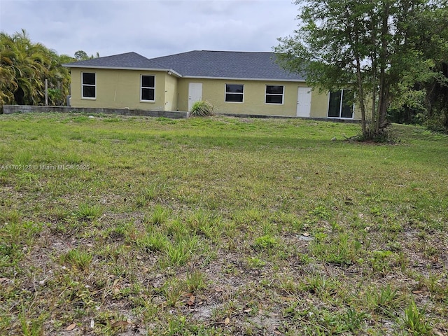 view of front facade featuring a shingled roof, a front yard, and stucco siding