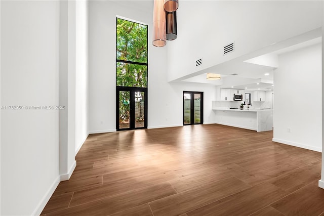 unfurnished living room with wood finished floors, visible vents, baseboards, french doors, and a towering ceiling