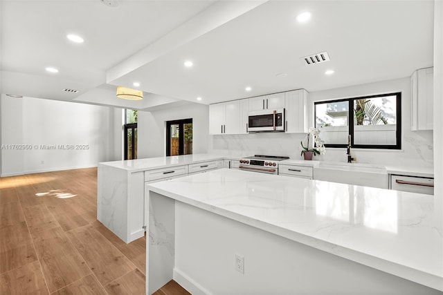 kitchen featuring a peninsula, light wood-type flooring, a wealth of natural light, and high end stove