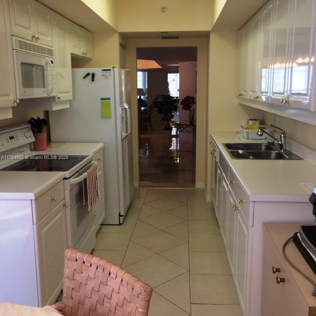 kitchen with white appliances, light tile patterned floors, a sink, light countertops, and white cabinetry