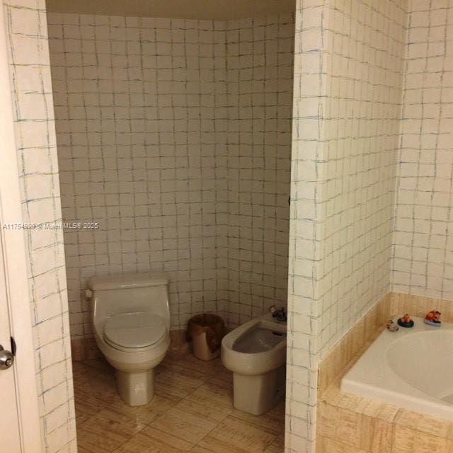 full bathroom with tiled bath, toilet, tile patterned floors, and tile walls