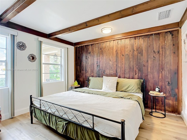 bedroom with beam ceiling, visible vents, wood walls, and light wood finished floors