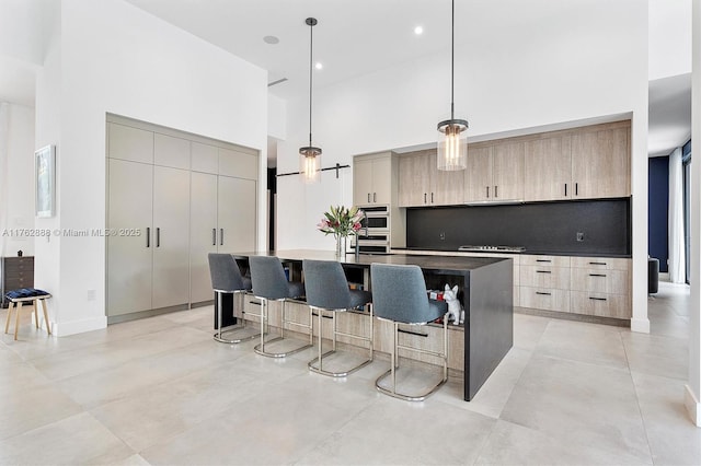 kitchen featuring light brown cabinets, a center island with sink, a kitchen bar, a towering ceiling, and modern cabinets