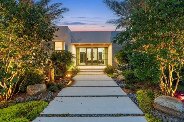 exterior entry at dusk with stucco siding and french doors