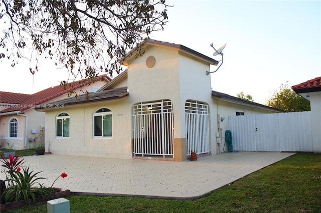 rear view of house featuring a gate, fence, stucco siding, a tiled roof, and a patio area