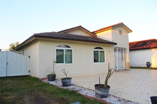 exterior space featuring a patio, a gate, driveway, stucco siding, and a tile roof