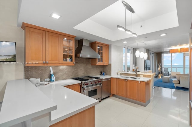 kitchen featuring wall chimney range hood, stainless steel appliances, a peninsula, light countertops, and decorative backsplash