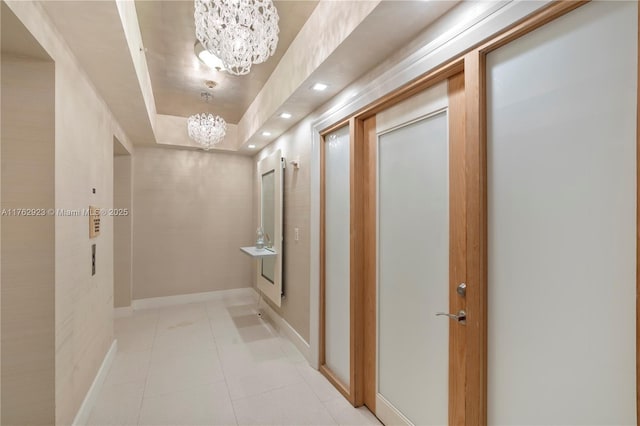 hall with light tile patterned floors, baseboards, recessed lighting, a raised ceiling, and a chandelier