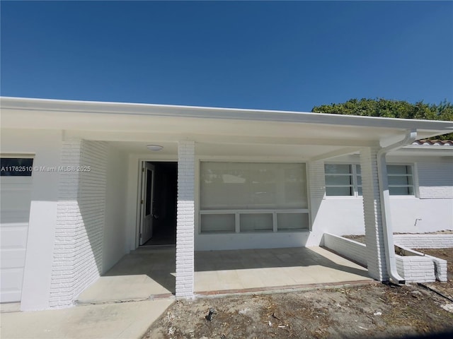 view of exterior entry with a garage and brick siding