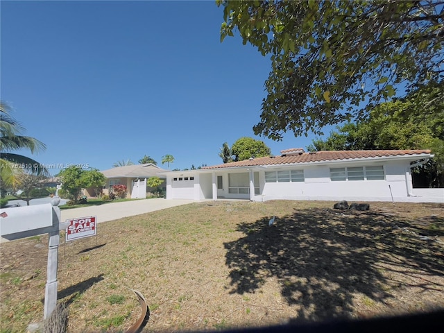 view of front of house featuring a tile roof, concrete driveway, a front yard, stucco siding, and an attached garage