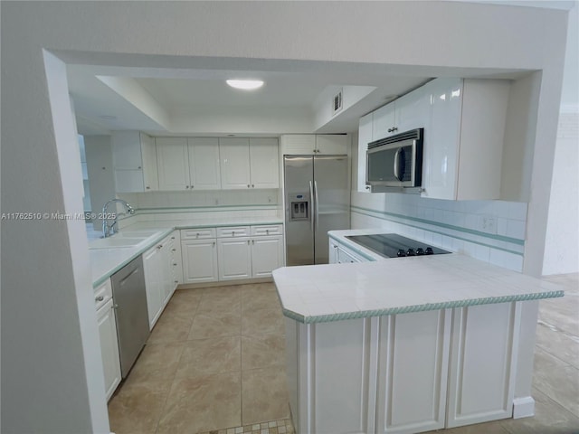 kitchen featuring a sink, appliances with stainless steel finishes, a peninsula, white cabinets, and light countertops