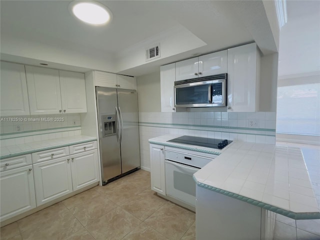 kitchen with visible vents, a peninsula, stainless steel appliances, decorative backsplash, and white cabinetry