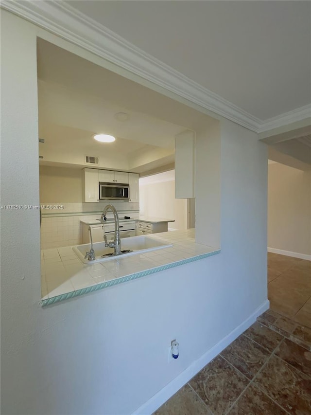 kitchen featuring visible vents, baseboards, white range with gas stovetop, crown molding, and stainless steel microwave