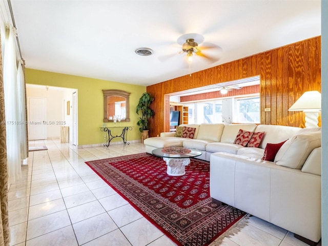 living area with light tile patterned floors, visible vents, wooden walls, and a ceiling fan