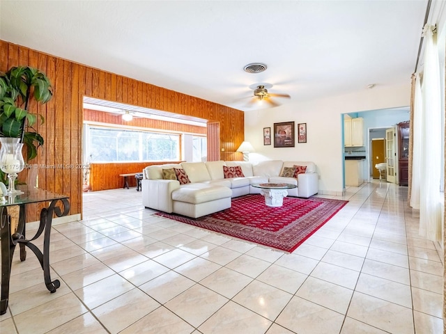 living room featuring light tile patterned floors, visible vents, wood walls, and ceiling fan