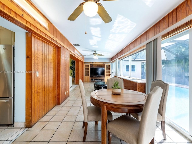 dining space with light tile patterned floors, built in features, visible vents, ceiling fan, and wood walls