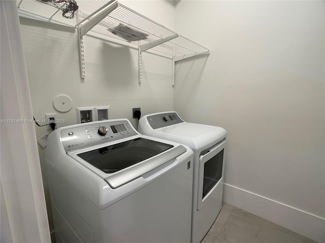 washroom featuring laundry area, washing machine and dryer, marble finish floor, and baseboards