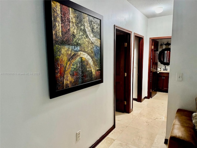 hall featuring baseboards, marble finish floor, and a textured ceiling