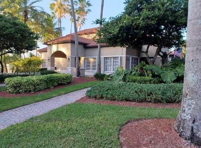 view of front of home featuring stucco siding, a tile roof, and a front yard