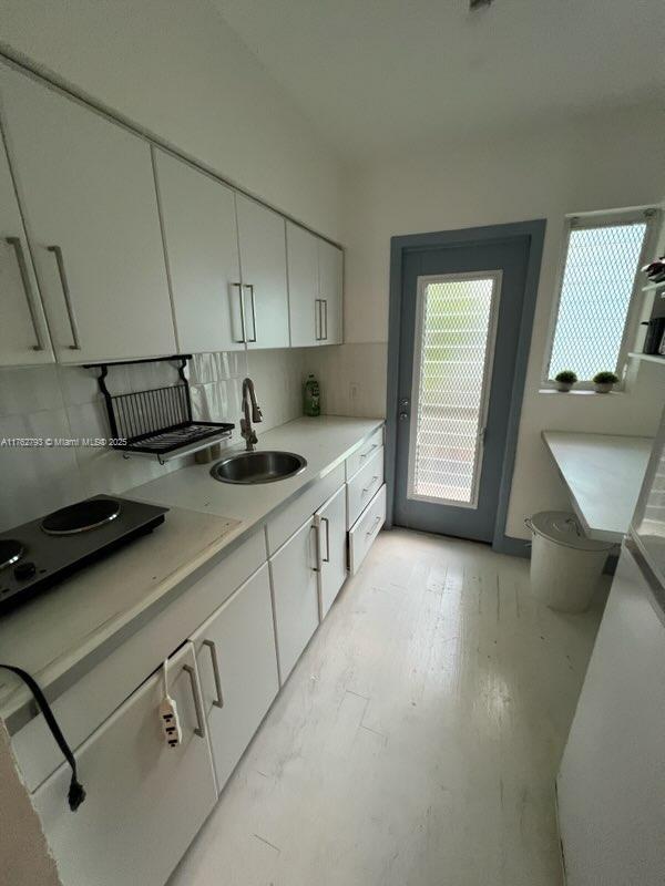 kitchen with a sink, tasteful backsplash, white cabinets, and light countertops