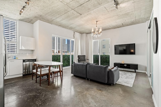 living area featuring a notable chandelier, track lighting, concrete flooring, and baseboards