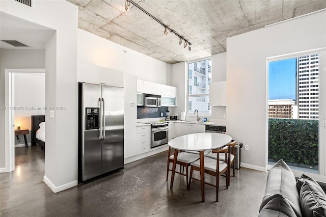 kitchen featuring baseboards, concrete floors, a sink, white cabinets, and appliances with stainless steel finishes