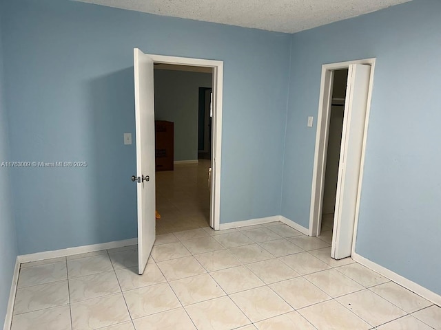 unfurnished bedroom featuring light tile patterned flooring, baseboards, and a textured ceiling