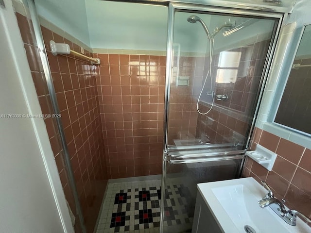 full bath with tile walls, a stall shower, vanity, and tile patterned flooring