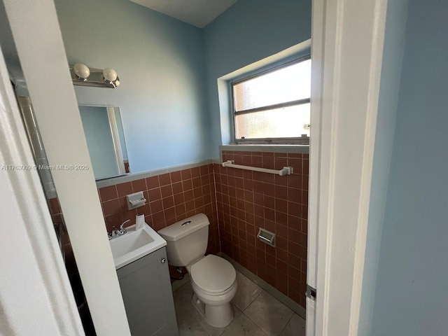 half bathroom with tile walls, toilet, wainscoting, tile patterned floors, and vanity