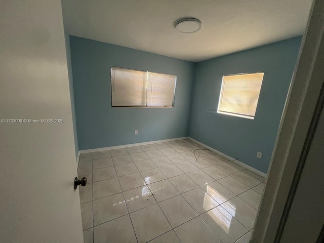 spare room featuring light tile patterned floors and baseboards