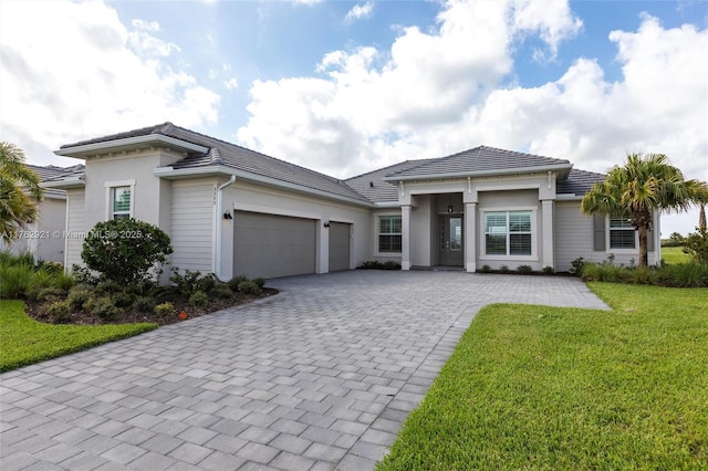 prairie-style home featuring stucco siding, a front lawn, a garage, a tiled roof, and decorative driveway