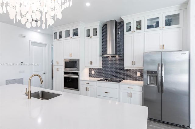 kitchen featuring a sink, decorative backsplash, light countertops, appliances with stainless steel finishes, and wall chimney range hood