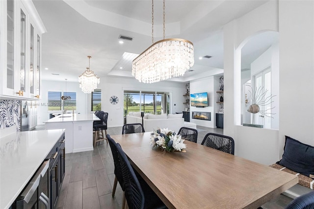 dining room featuring a glass covered fireplace, visible vents, a raised ceiling, and an inviting chandelier