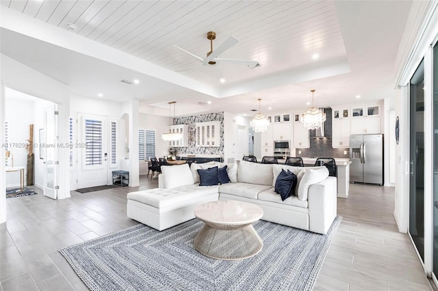 living room featuring recessed lighting, wooden ceiling, ceiling fan with notable chandelier, and a tray ceiling