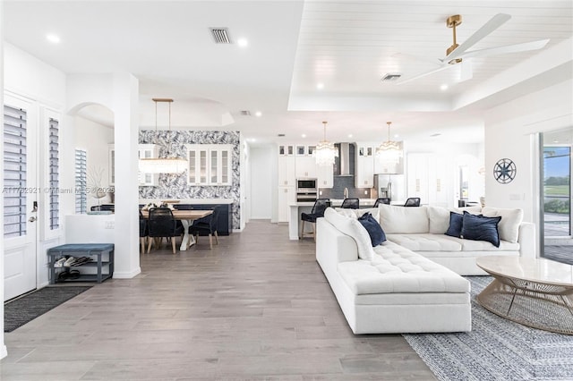 living area with visible vents, light wood finished floors, a tray ceiling, recessed lighting, and ceiling fan with notable chandelier