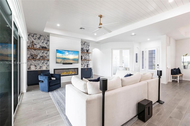 living room featuring wood finish floors, a tray ceiling, recessed lighting, french doors, and a glass covered fireplace