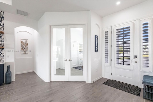 foyer entrance featuring visible vents, baseboards, french doors, wood finished floors, and arched walkways