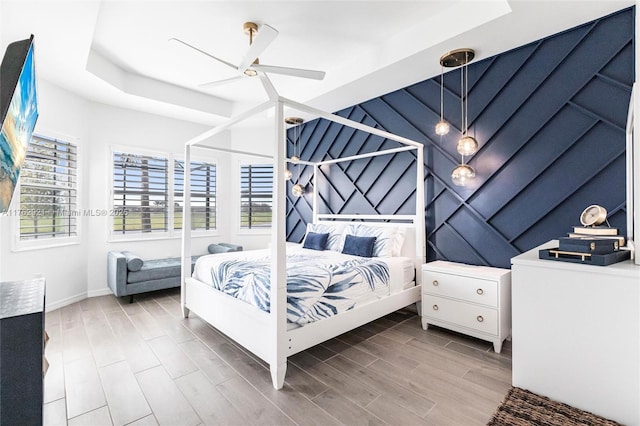 bedroom with a ceiling fan, a raised ceiling, multiple windows, and wood finished floors