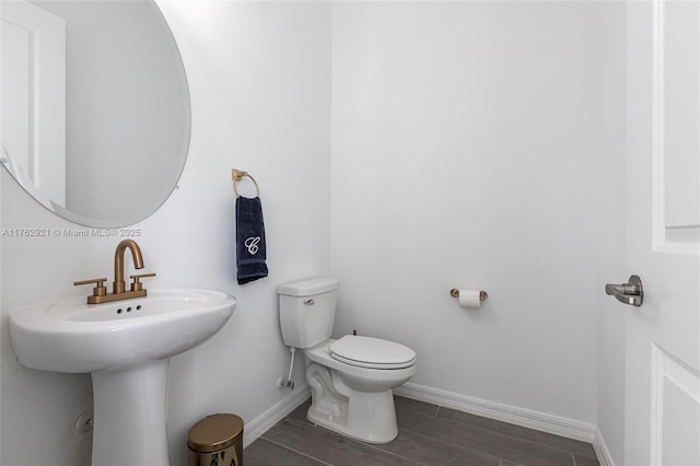 bathroom with toilet, wood finished floors, baseboards, and a sink