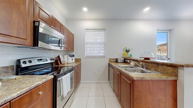 kitchen featuring brown cabinetry, appliances with stainless steel finishes, a peninsula, and a sink