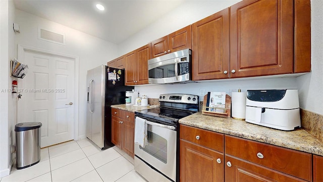 kitchen with visible vents, brown cabinets, stainless steel appliances, light tile patterned floors, and light stone countertops