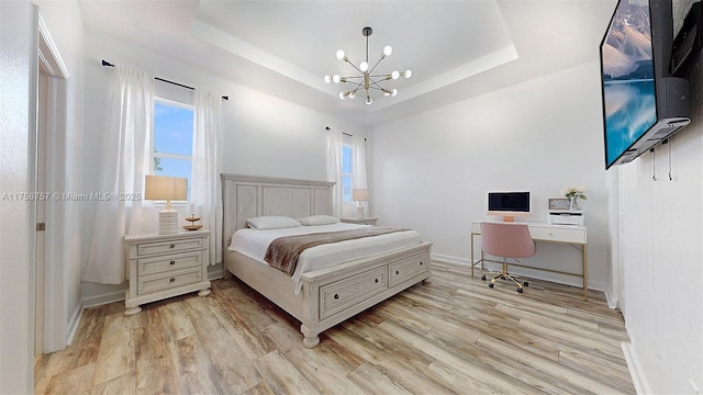 bedroom featuring a notable chandelier, light wood-style flooring, a raised ceiling, and multiple windows