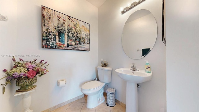 half bath with tile patterned floors, toilet, baseboards, and a sink