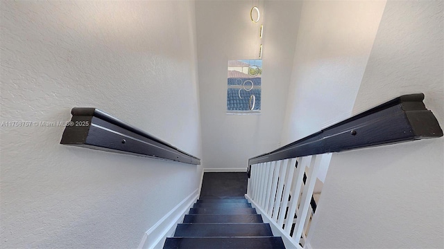 staircase featuring wood finished floors, baseboards, and a textured wall