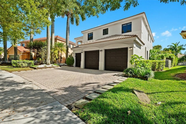 mediterranean / spanish-style home featuring stucco siding, a front lawn, decorative driveway, a garage, and a tiled roof