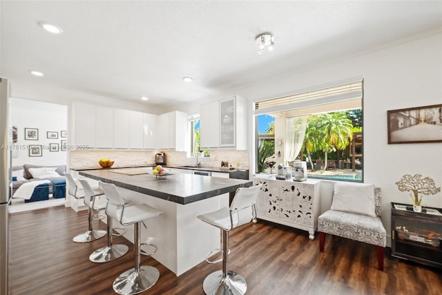 kitchen with backsplash, a kitchen bar, glass insert cabinets, and dark countertops