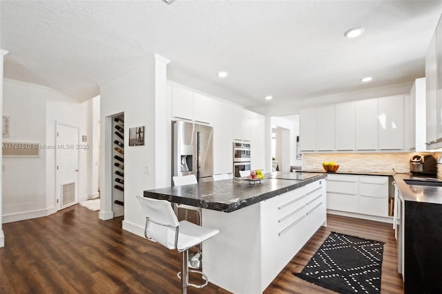 kitchen with a center island, a kitchen bar, decorative backsplash, dark wood-style floors, and stainless steel appliances