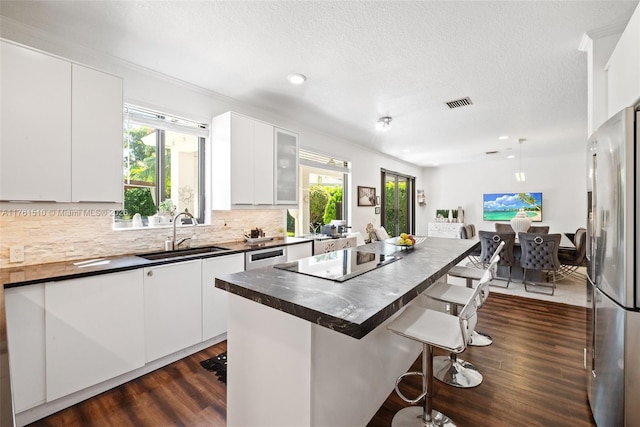 kitchen with a breakfast bar, a sink, tasteful backsplash, freestanding refrigerator, and black electric cooktop